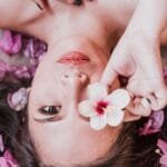 Elegant photoshoot featuring a woman holding a pink flower amidst petals.